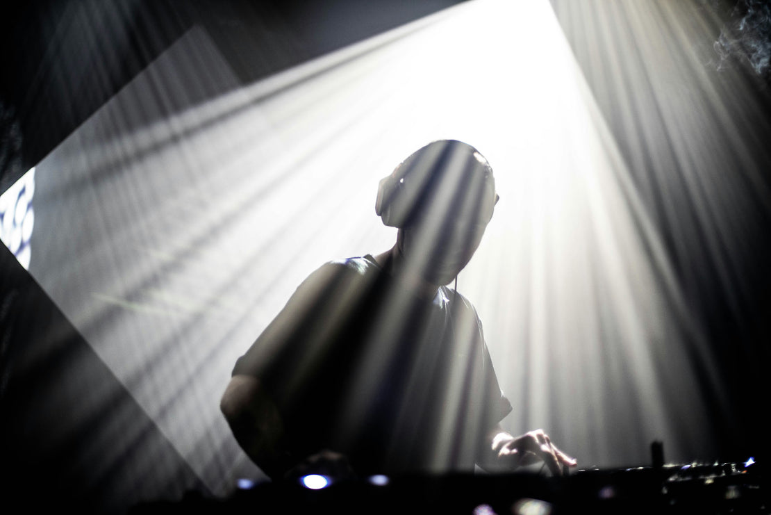 DJ under spotlight with headphones on, using DJ mixer deck.