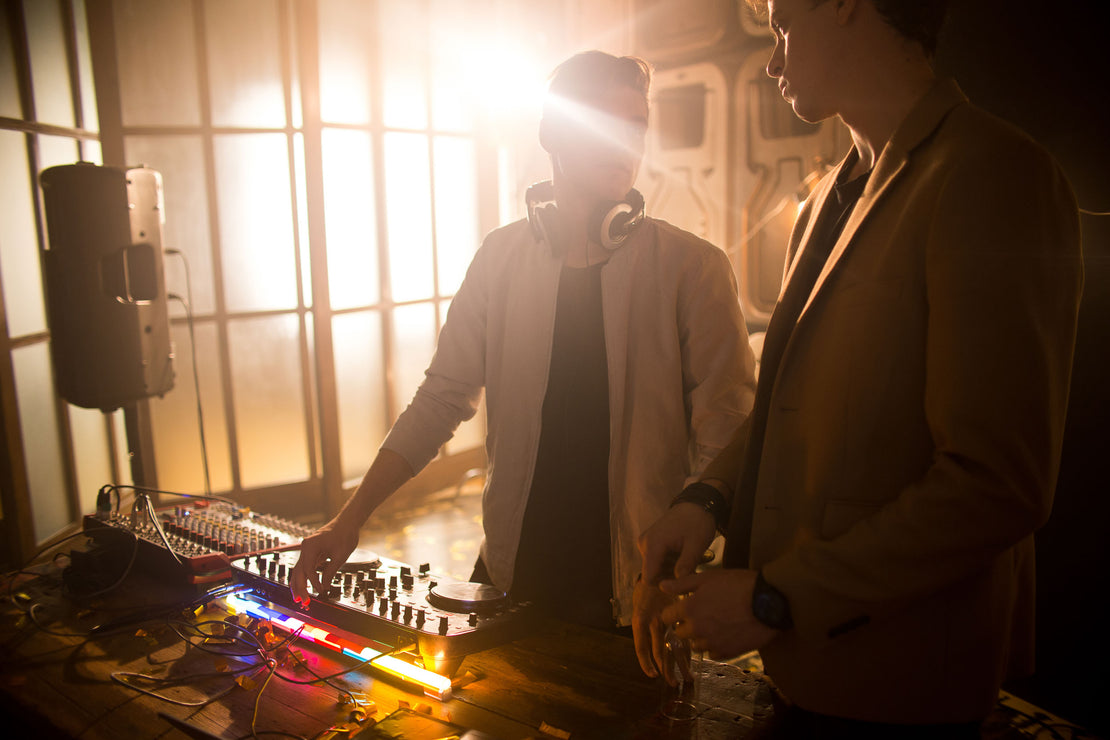 Two men standing and talking at DJ controller deck.